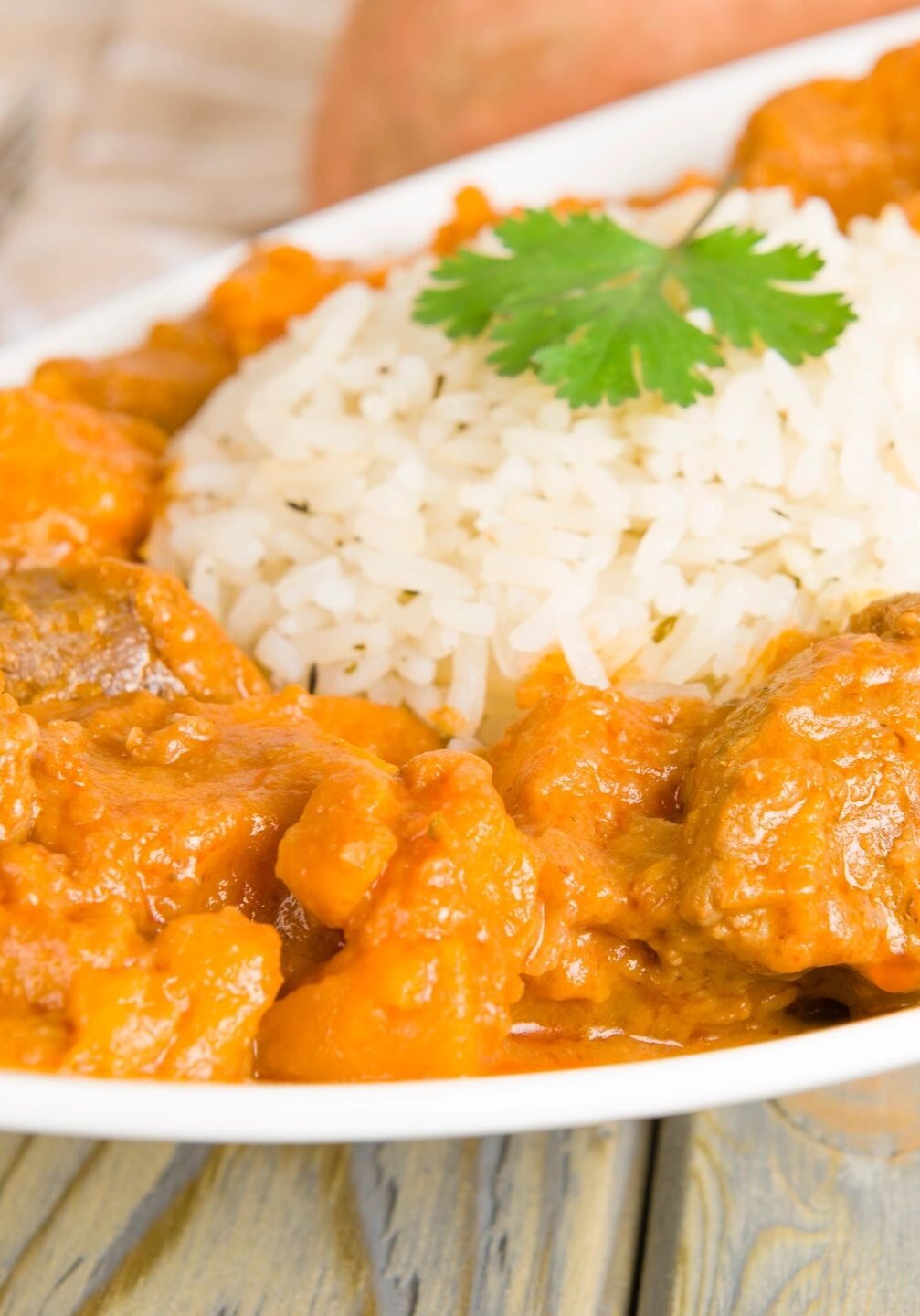 Plate of creamy chicken curry served with white rice and garnished with cilantro.
